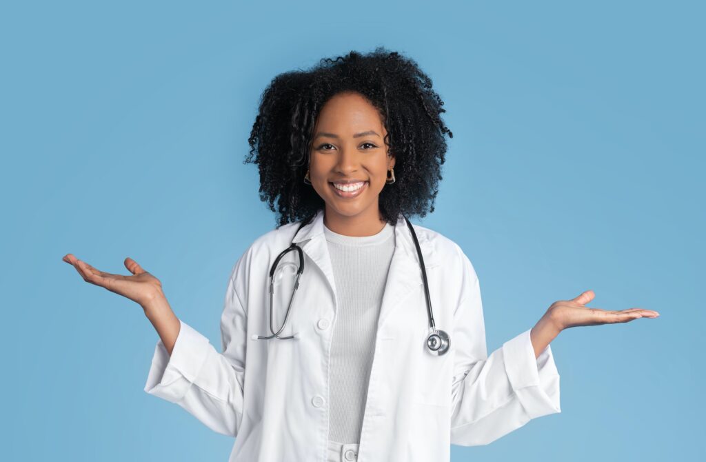 Cheerful young black lady doctor therapist in white coat hold free space in hands