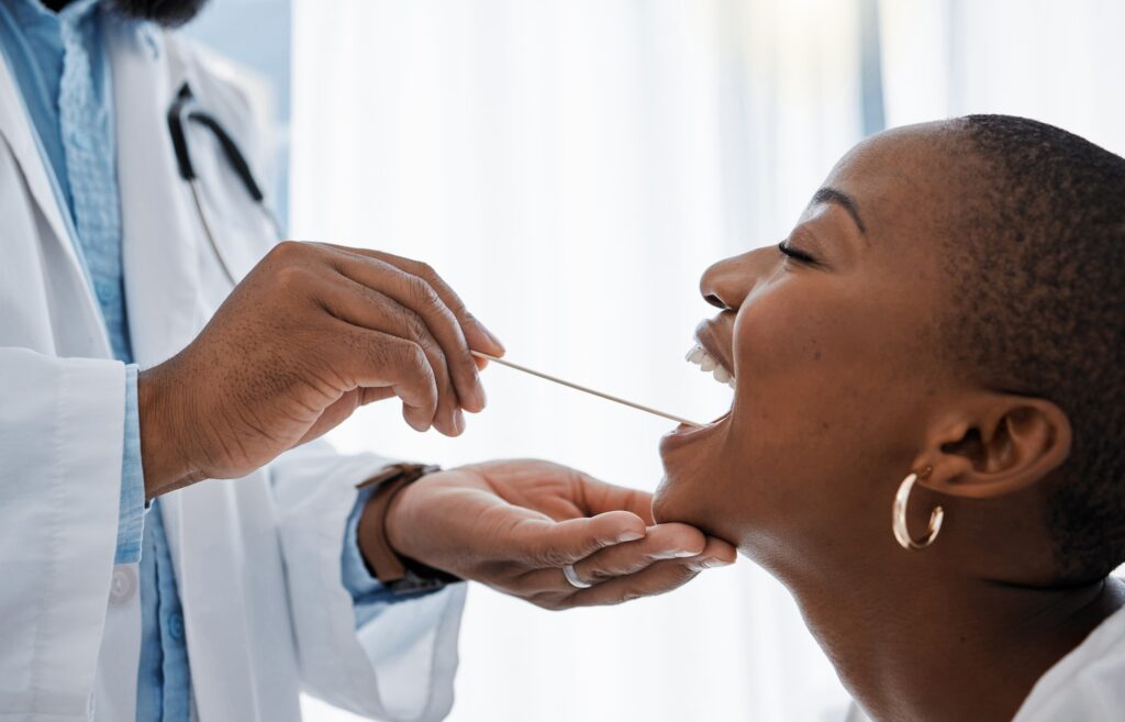 Doctor, otolaryngologist or dentist with a medical instrument checking the throat for tonsils or or