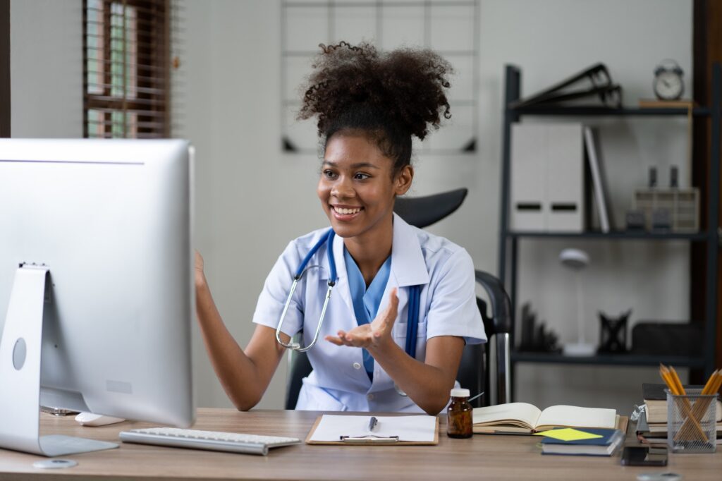 Portrait of female African American doctor sitting in her office at clinic. working with dewsktop
