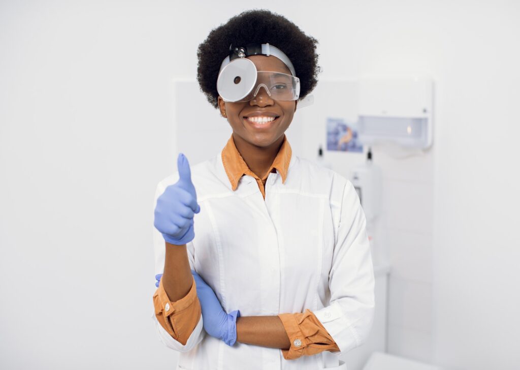 Portrait of young afro american lady otolaryngologist with a medical mirror on her head, smiling and
