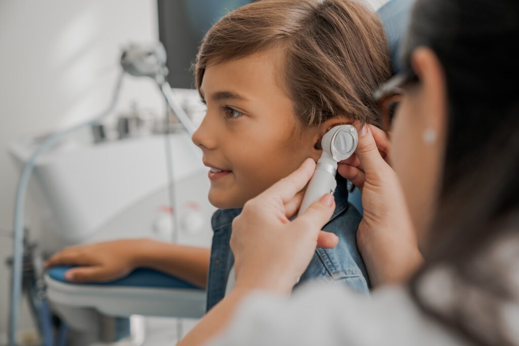 Side view shot of female doctor examining boy's ear with otoscope