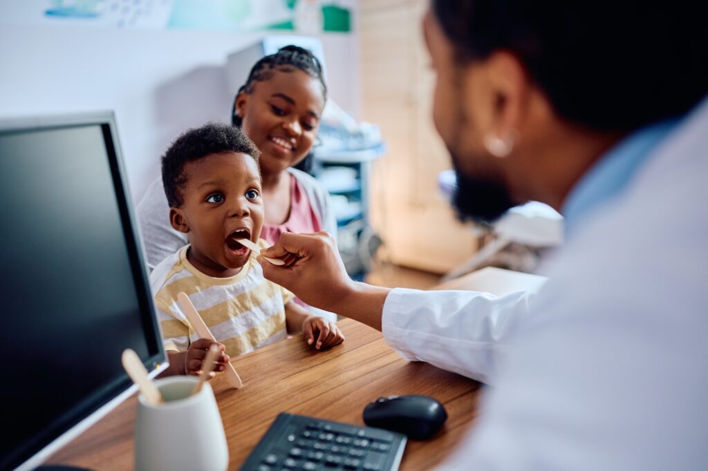 Small black boy having throat exam while being with his mother at pediatrician's.